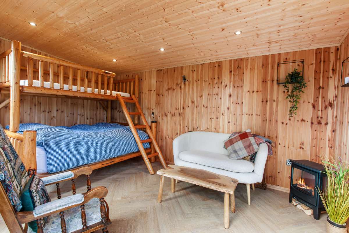 Garden cabin interior with log-frame bunk bed, sofa and wood-burning stove